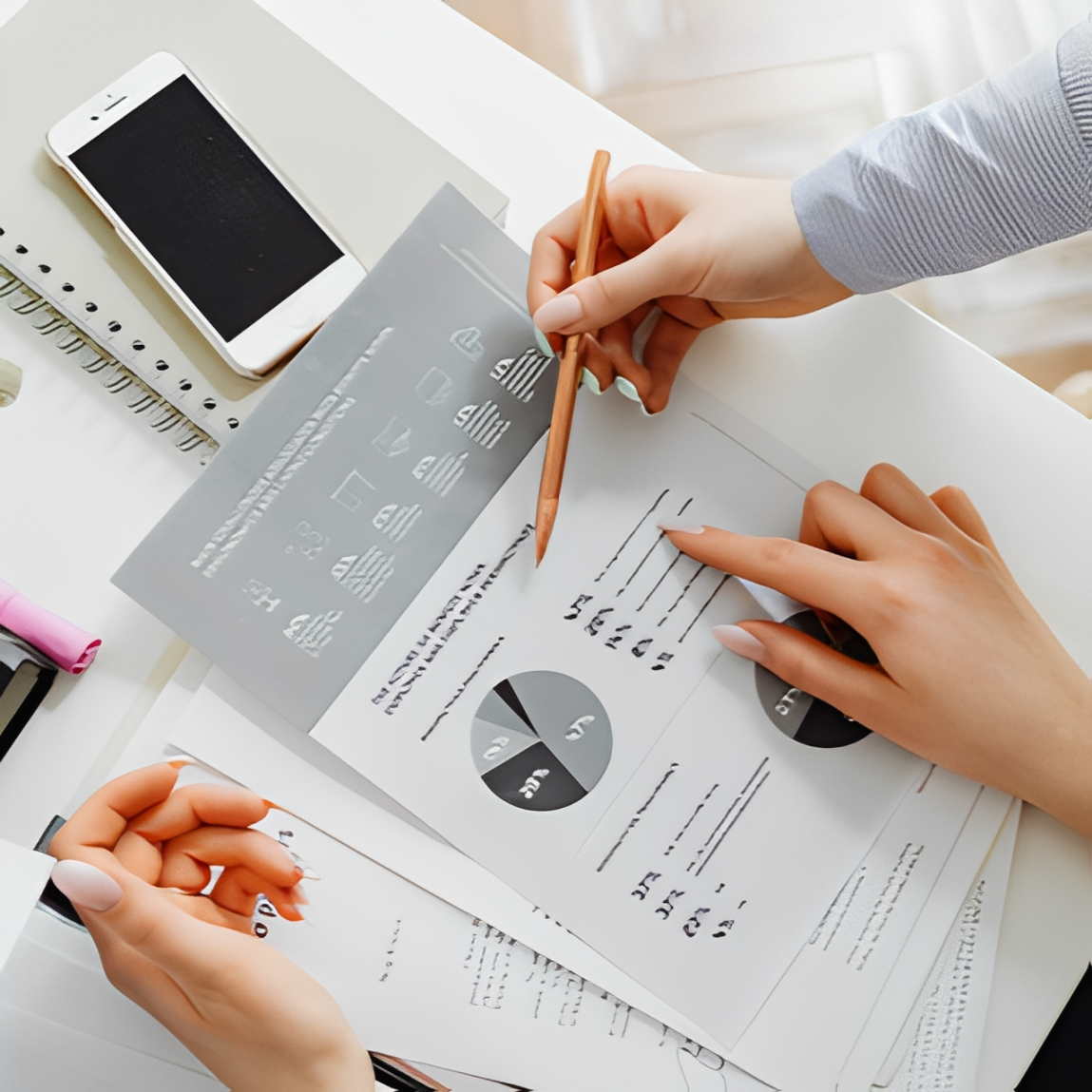 データ分析資料を指さしながら打ち合わせをする2人の手元。グラフや数値をもとに業務を見える化している様子を表す。